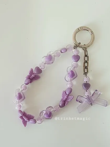 A pastel purple beaded keychain with butterfly and heart beads, plus a larger bow charm. It's a perfect example of the soft and sweet kawaii style.