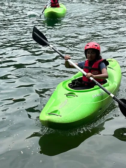 A participant in a green whitewater kayak practices her paddling technique. These specialized kayaks are used for navigating more challenging river conditions.