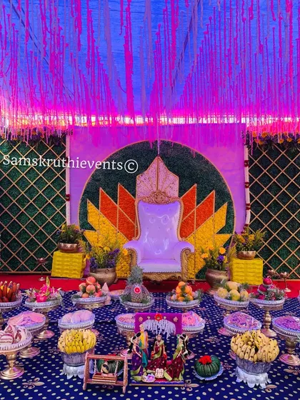 A colorful baby shower setup with a lotus backdrop and a unique blue dotted floor covering. The dramatic lighting enhances the vibrant colors of the flowers and decorations.