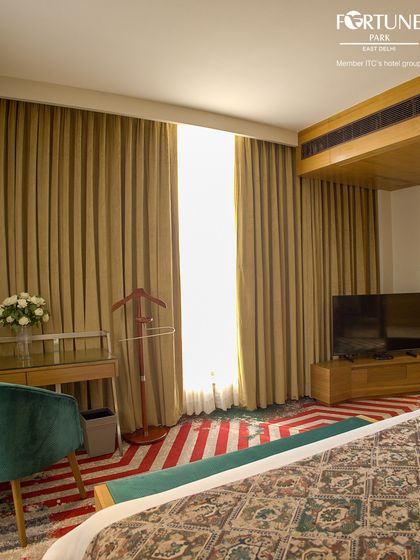 This angle showcases the room's functional layout, including the work desk and chair, television console, and full-length curtains for privacy.