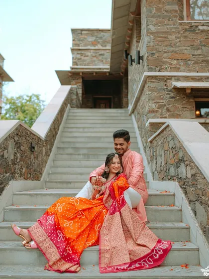 A lovely portrait of the couple seated on the steps of their destination wedding venue, their colorful outfits vibrant against the stone architecture.
