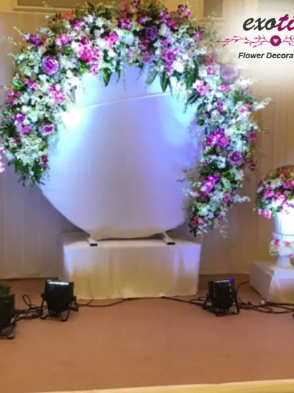 A modern and stylish photo booth for your engagement or reception. This circular backdrop is framed with a lush arch of purple and white orchids, creating a perfect spot for guests to capture memories.