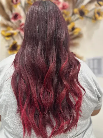 This client is rocking a fiery red ombre. The color transitions from a darker, natural root to bright, vivid red ends, styled in loose waves for a dramatic effect.
