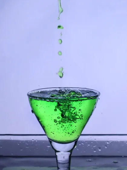 A continuous pour of green liquid into a glass, capturing the bubbles and motion within the drink for a lively effect.