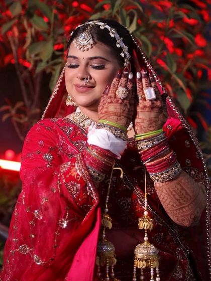 A beautiful candid moment of the bride. The soft-focus background highlights her radiant HD makeup, intricate jewellery, and the detailed henna on her hands.