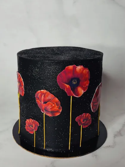 A still shot of the stunning poppy cake. The vibrant red of the edible wafer paper poppies stands out beautifully against the shimmering black buttercream.