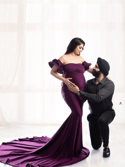 A classic and adoring couple pose. The dad-to-be kneels to look up at his partner, who is radiant in a purple gown, creating a sweet and romantic portrait.