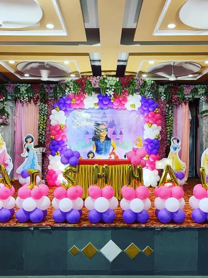 A full stage setup for a princess party, complete with balloon pillars spelling out the birthday girl's name, "VATSHALY," and multiple princess cutouts.
