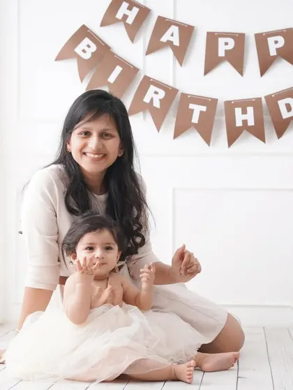 A lovely mother-daughter moment captured during a first birthday photoshoot, with both smiling in a bright, white studio.