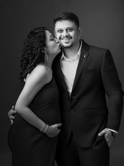 A playful and loving moment captured in black and white, as the mom-to-be gives her partner a sweet kiss on the cheek.