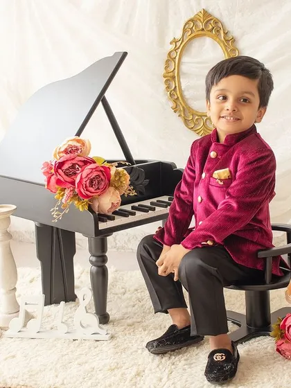 A handsome young man dressed in a velvet jacket, posing confidently by the miniature piano for a classic portrait.
