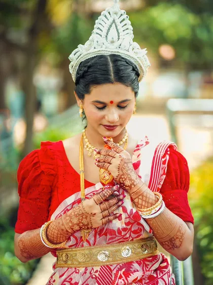 A serene portrait of the bride in her traditional red and white saree, her hands adorned with mehndi.