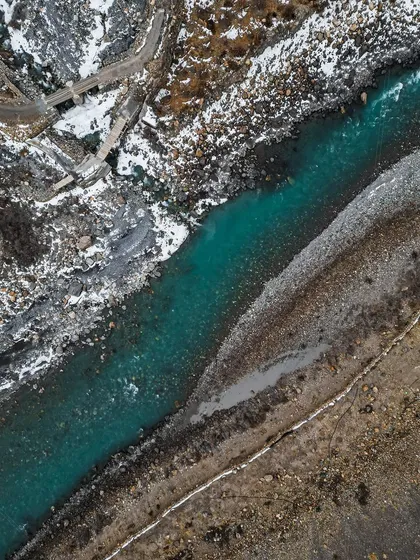 A top-down aerial shot of the turquoise river in Poh, contrasting with the snow and rocky banks.