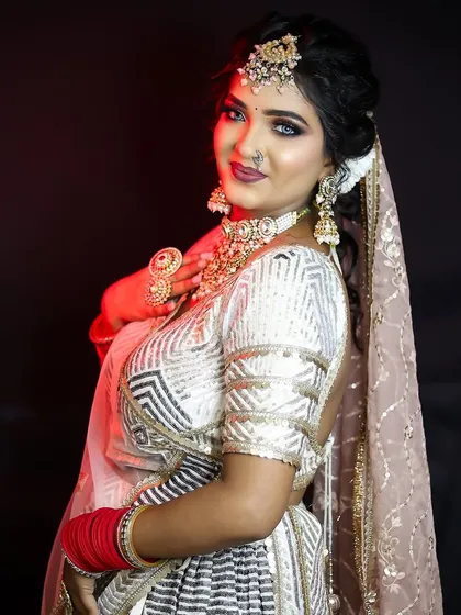 A modern bride in a white and silver lehenga. The makeup is glamorous with a dark, smokey eye and a bold lip, perfect for a reception or evening event.