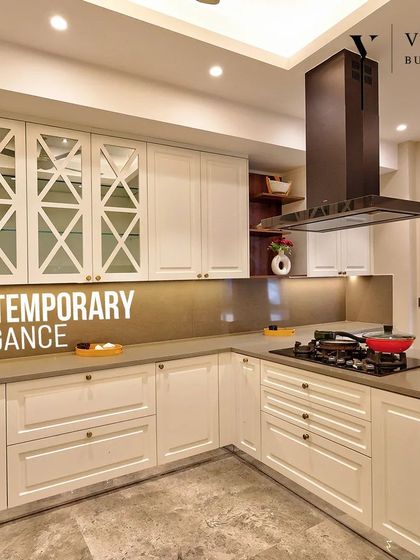 This kitchen exudes contemporary elegance. The white shaker cabinets with cross mullion glass doors, combined with a modern black chimney and under cabinet lighting, create a look that is both classic and fresh.