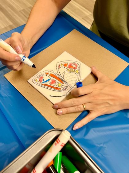 A participant carefully colors a butterfly design onto a foam plate during our printmaking workshop for kids and adults.