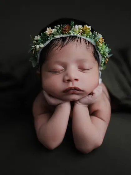 This classic 'chin on hands' pose is a favorite for showcasing a newborn's delicate features. We use dramatic, low-key lighting and soft wraps to create a serene and artistic portrait.
