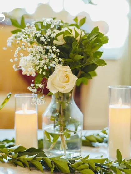 A simple, elegant centerpiece of white roses and baby's breath with candles, perfect for creating a warm and intimate atmosphere at home.