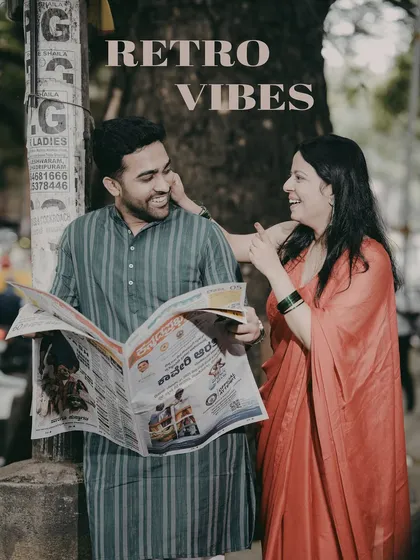 A retro-themed pre-wedding photo where the couple shares a laugh while reading a newspaper, creating a candid and nostalgic scene on a Bangalore street.