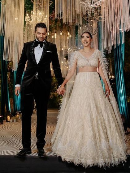 A vision in our ivory lehenga, intricately embellished and finished with delicate feather accents. The floor-sweeping cape sleeves add a dramatic yet graceful touch to this statement of refined luxury.