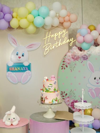 The two-tier garden bunny cake as part of the full birthday party decor. It fits perfectly with the pastel balloon arch and backdrop.