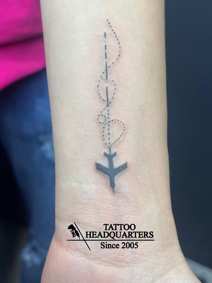 A minimalist airplane tattoo with a dotted flight path that forms two hearts, symbolizing a love for travel.