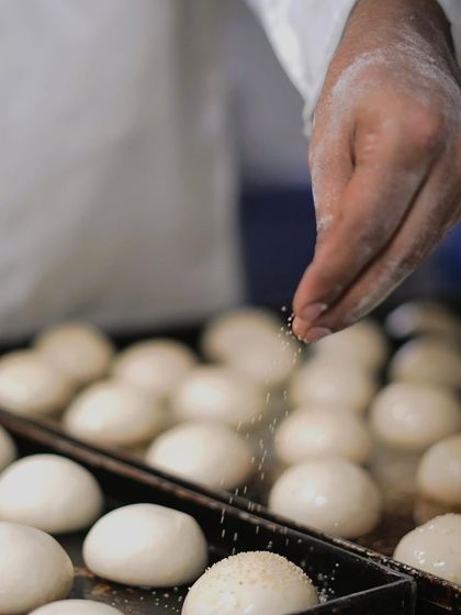 The baker's touch. A chef sprinkles sesame seeds onto fresh dough balls before they go into the oven, a simple step that adds so much to the final product.