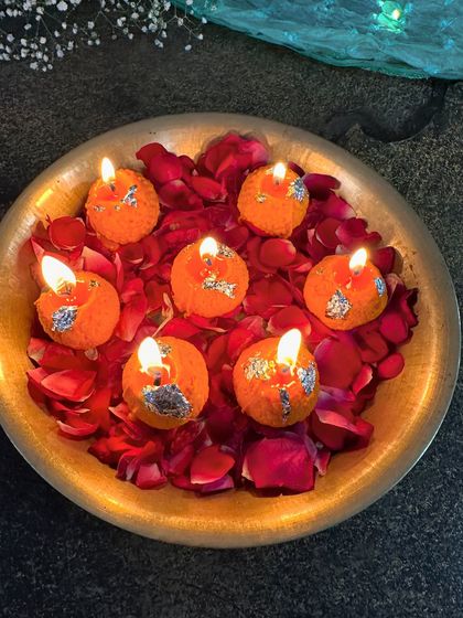 My laddoo soy candles lit and arranged in a traditional brass urli with rose petals. The warm glow from each candle creates a beautiful and festive centerpiece.