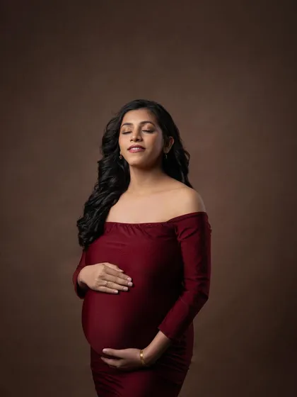 A peaceful close-up, focusing on the connection between mother and baby. The rich red color of the gown adds warmth and love to the image.