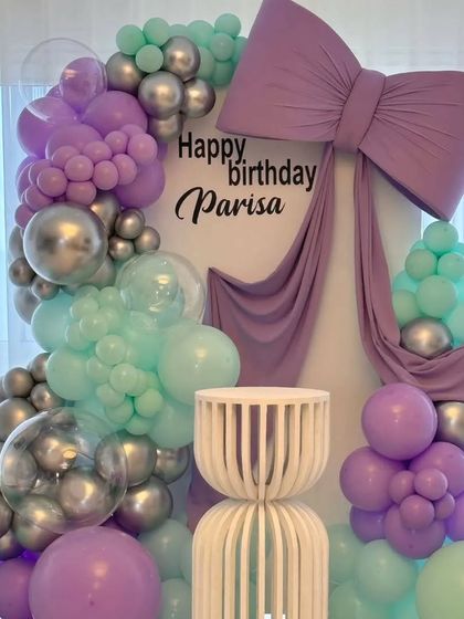 A detailed shot of the elegant birthday decor with a large sculpted bow. The mix of balloon sizes and the inclusion of clear balloons filled with smaller silver ones adds texture and depth.