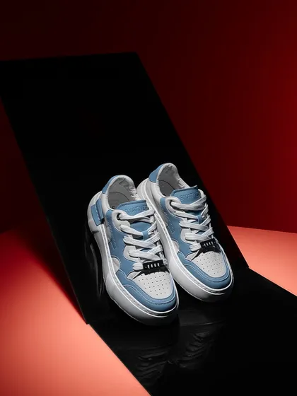 A sleek, graphic shot of light blue sneakers on a reflective black surface against a red background. The clean lines and bold colors give this image a very modern and sharp feel.