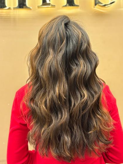 A back view of a client's long, wavy hair with fresh highlights. The style is glamorous and full of volume, showcasing the beautiful color work.