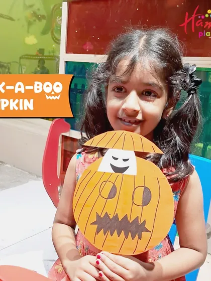A smiling girl displays her handmade peek-a-boo pumpkin craft. It's a simple yet fun activity that lets kids create their own friendly ghost surprise.