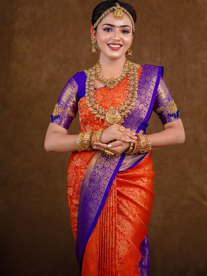 An orange and royal blue Kanchipuram saree styled for a photoshoot. The contrast is striking, and the drape is kept traditional to highlight the saree's grandeur.