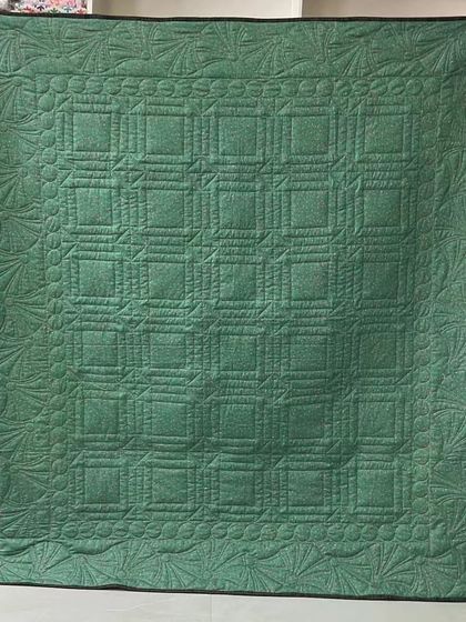 The solid green back of a quilt, showcasing a complex pattern of custom ruler work and free-motion feathers.