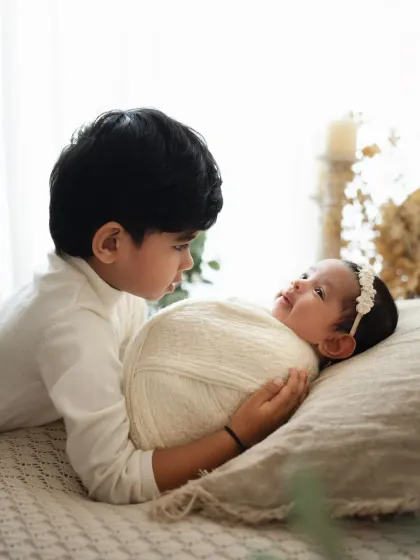 A big brother lies next to his swaddled newborn sister, watching over her. This is a wonderful way to capture the beginning of their journey together.