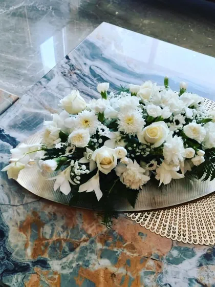 This elegant centerpiece features a bed of white roses, carnations, and daisies arranged on a silver platter. It's a simple yet sophisticated addition to a dining table or coffee table for any celebration.