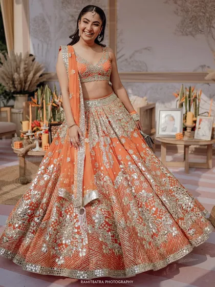 A full-length shot of the bride looking radiant and happy in her vibrant orange Abhinav Mishra lehenga.
