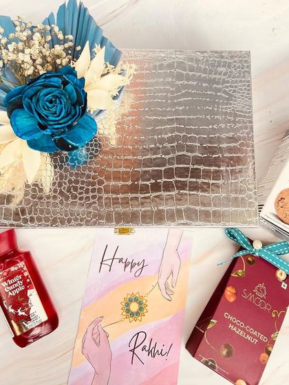 A chic trunk box hamper for a sister this Rakhi. The silver crocodile-textured box is decorated with a stunning blue rose and filled with her favorite cookies and skincare.