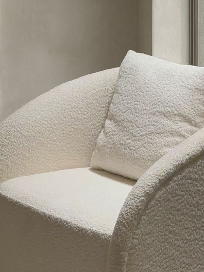 A close up on the textured fabric and curved arm of the contemporary armchair, highlighting the quality of the upholstery and the inviting form.