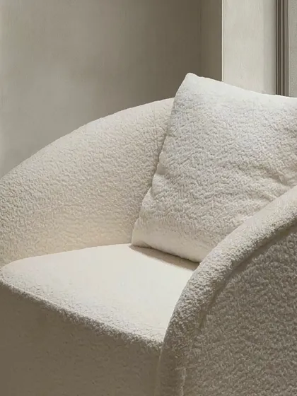 A close up on the textured fabric and curved arm of the contemporary armchair, highlighting the quality of the upholstery and the inviting form.