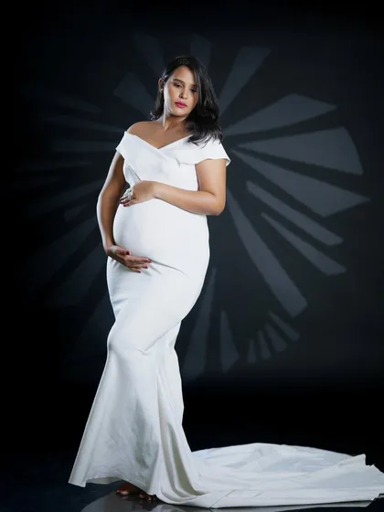 This portrait showcases an elegant, off-the-shoulder white gown that beautifully drapes over the baby bump. The dramatic studio lighting creates a sophisticated and timeless look, focusing entirely on the mother-to-be.