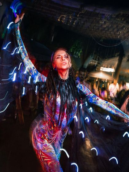 An upward shot of the psychedelic light cape performance, capturing a moment of spiritual intensity. The motion blur creates a beautiful effect of flowing light.