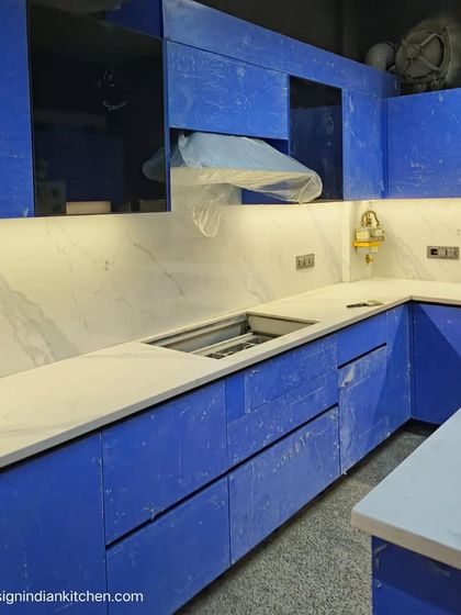 A view of the cooking area under installation, with the protective film still on. The design features a white marble backsplash that complements the vibrant blue shutters beautifully.