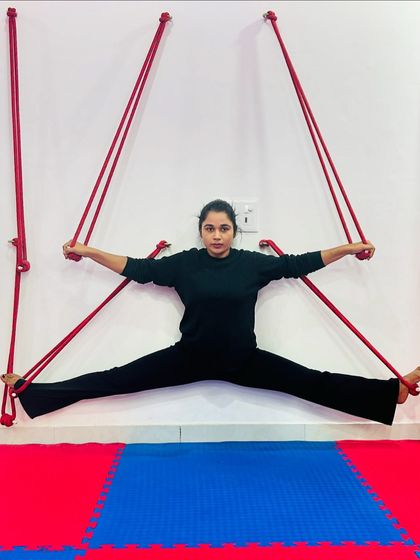 This student demonstrates a full split against the wall, using the ropes for balance and support. It's a powerful stretch for the hamstrings and hip flexors.
