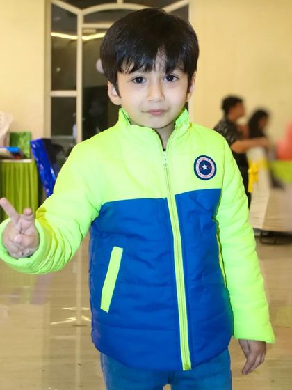 A young boy in a colorful jacket gives a peace sign to the camera, showing his fun personality.