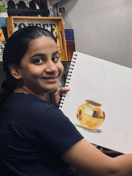 Nothing makes us happier than seeing a student proud of their progress. Here, a student from our elementary batch shows off her beautifully rendered metal pot, mastering light and shadow.