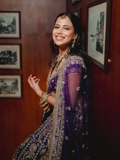 A bride ready for her sangeet in a vibrant purple lehenga. The makeup is glamorous with a touch of shimmer, perfect for a night of dancing and celebration.