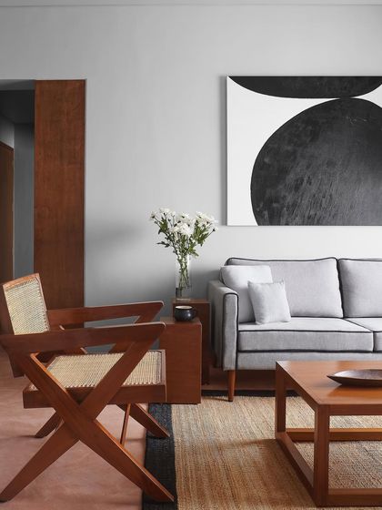 A living room scene with a custom grey sofa and a classic wooden armchair with cane details. I believe in mixing materials and styles to create a space that feels collected and personal.