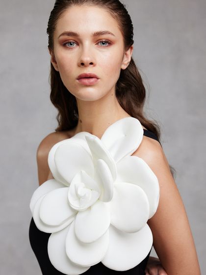 A minimalist portrait where the fashion statement is a single, oversized white flower accent on a simple black top. This look demonstrates how a single, sculptural element can define an entire image.